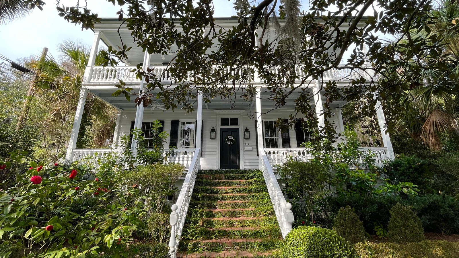 A brick walkway leads up to a two-story white house. Bushes line each side of the walk. 