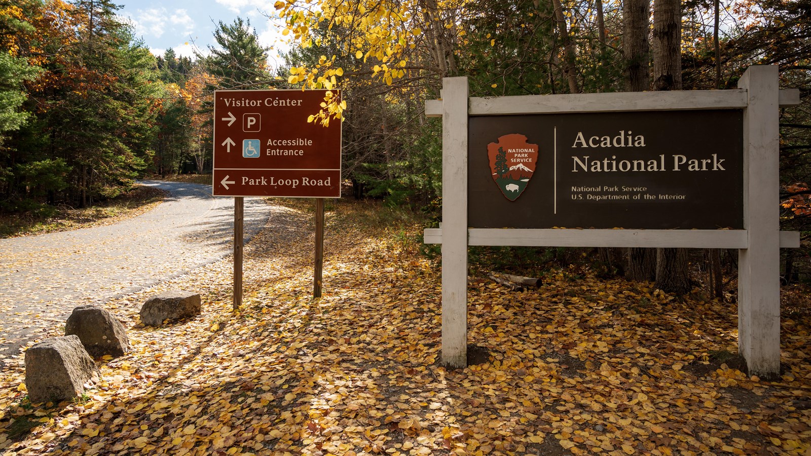 Two large road signs beside a road, one with the park name, the other points to accessible entrance