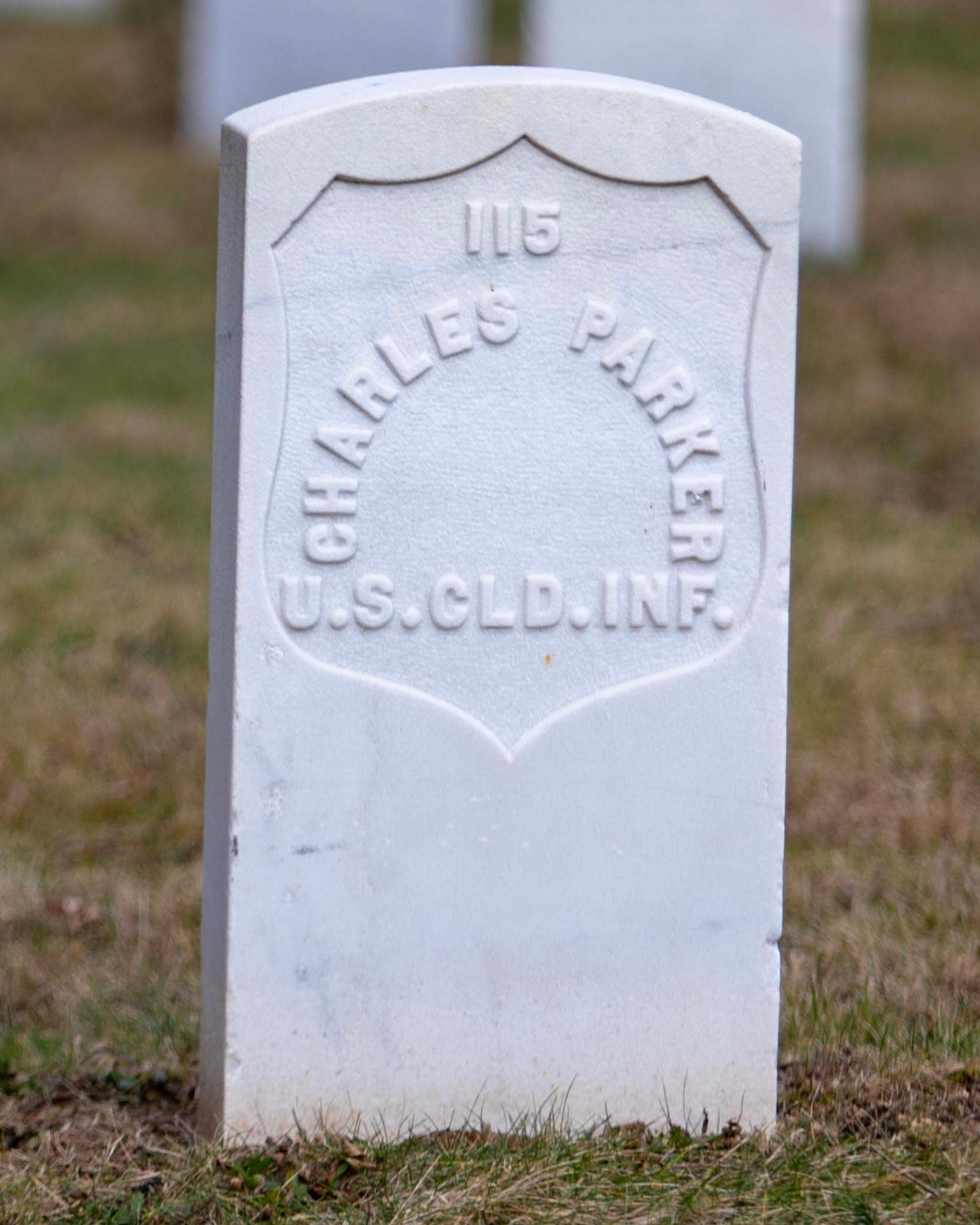 The gravestone of Charles Parker is a white marble stone with a curved top edge among other graves.