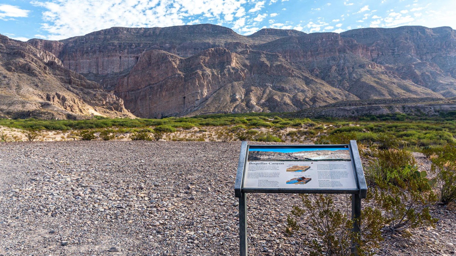 A metal sign sits on the edge of a bluff overlooking massive limestone walls cut by the Rio Grande.