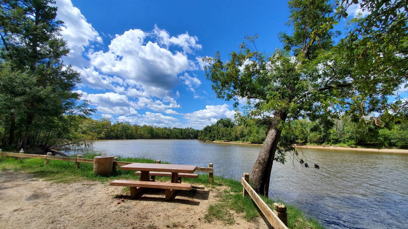 picnic table and trash can next to a wide river