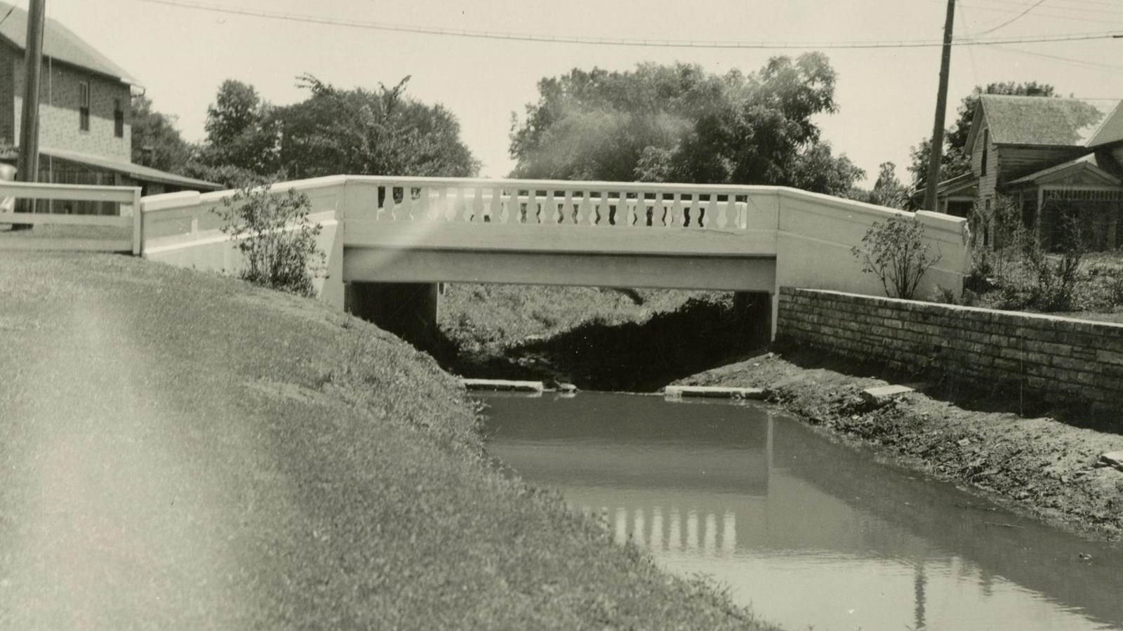 A 1931 photo depicts a concrete bridge spanning a small town creek.
