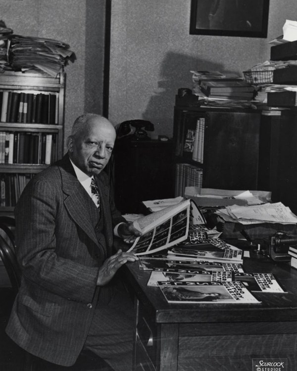 Carter G. Woodson sits at his desk looking through ASNLH Bulletins.