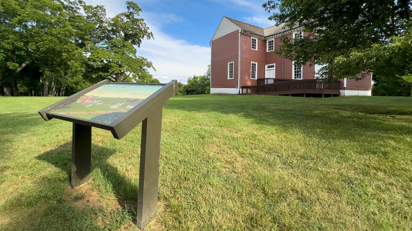 A park sign on a lawn in front of a 2-story red house.