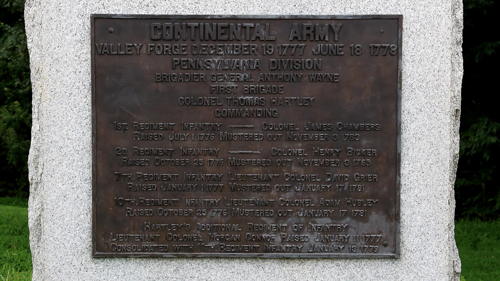 A large, smoothed granite block with bronze plaque, sides and bottom rough.