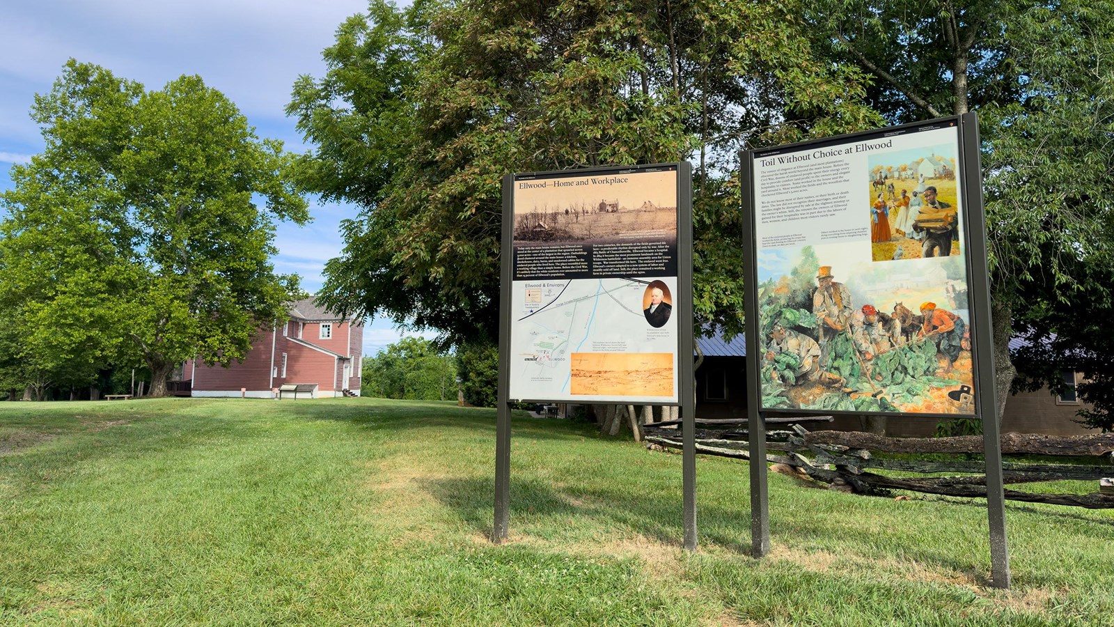 Two upright interpretive signs in front of a 2-story red plantation house.