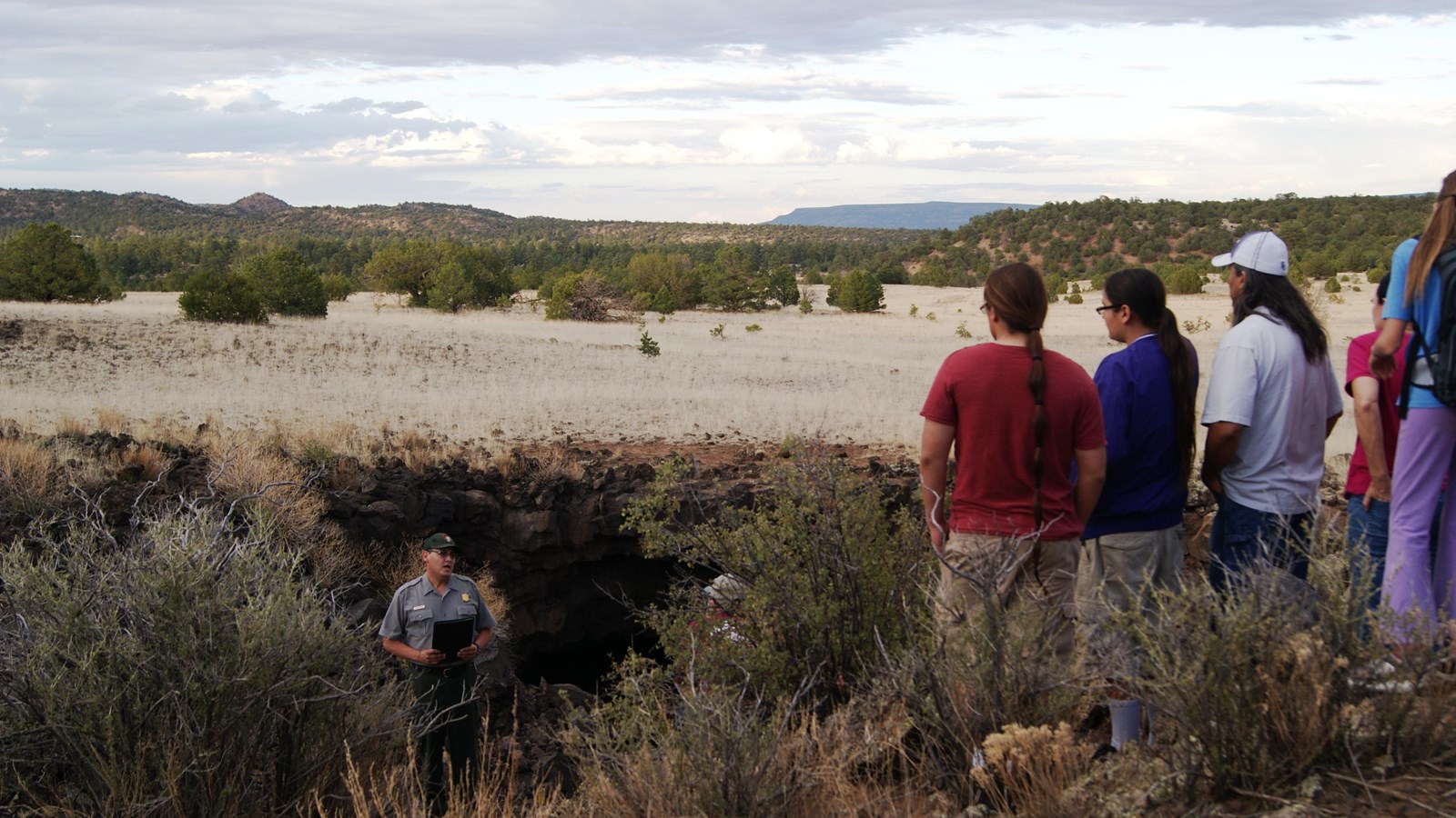 5 people stand watching a park ranger in front of the opening of a cave