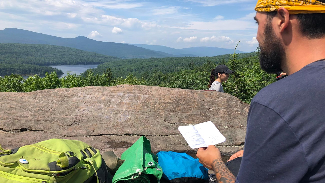 A man before a mountain vista looks over a map.