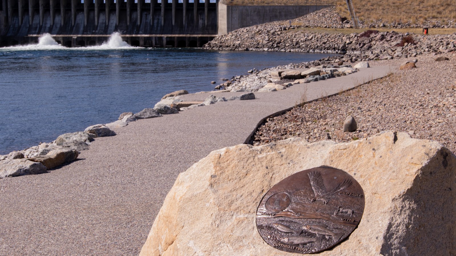 A bronze mediallion placed on a large boulder with the dam in the background.