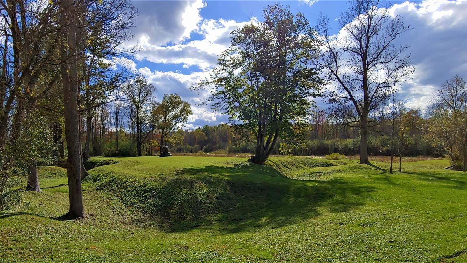 A grassy, shaded area with fort-shaped undulations in the ground.