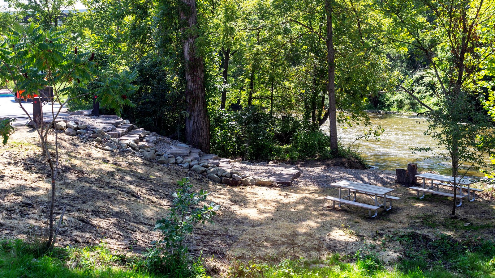 A stone staircase descends a wooded riverbank down to the water; two picnic tables to the right.