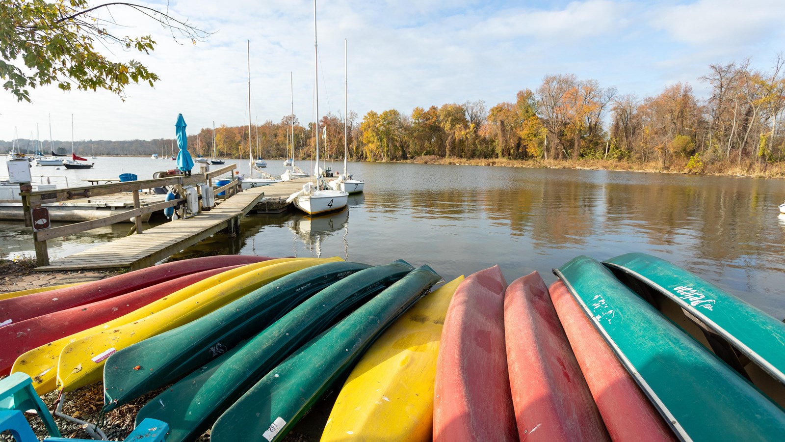 14 canoe boats are flipped upside down and stacked atop each other in front of a boat dock.