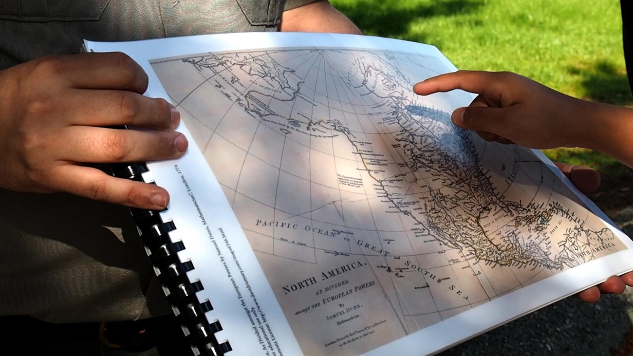 A child\'s hand points to a map that a ranger is holding