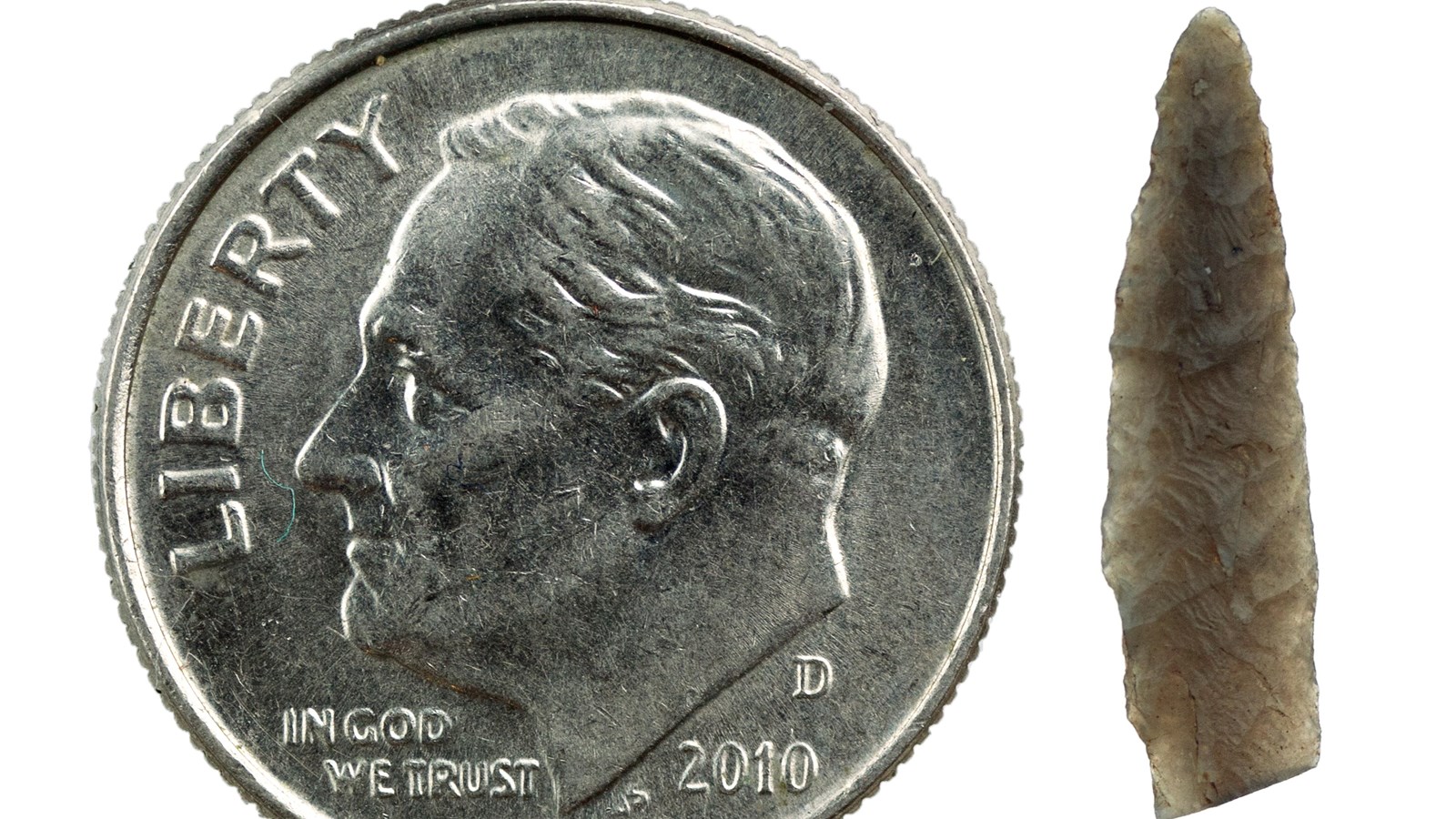A carved pointed stone tool next to a U.S. dime showing they are the same size.