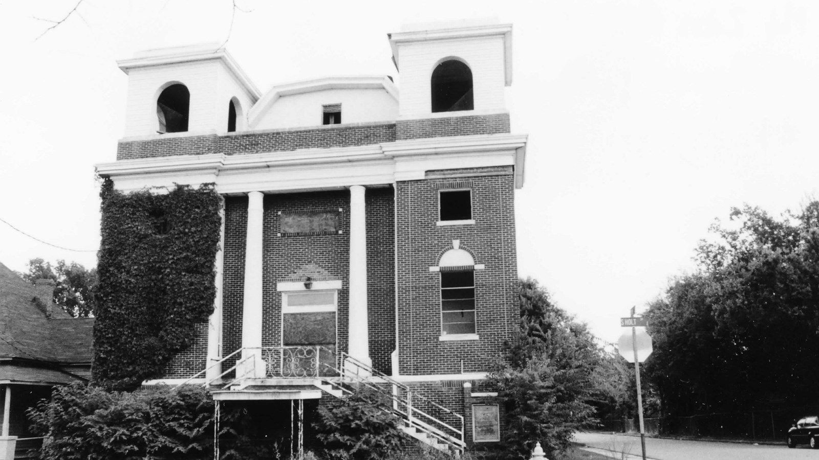 Brick classical revival-style church, with vegetation growing outside