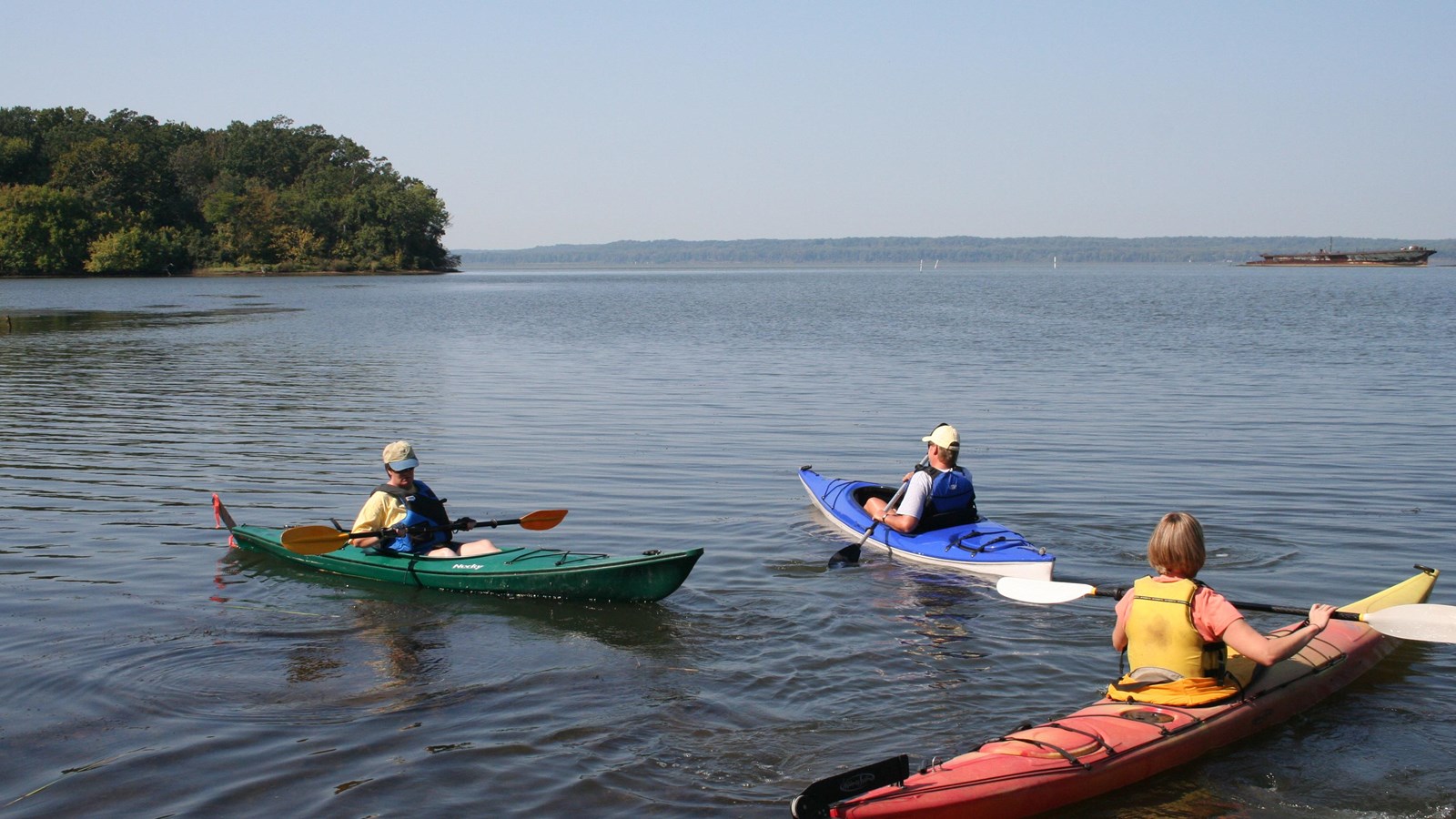 Three kayakers on a wide body of water. 