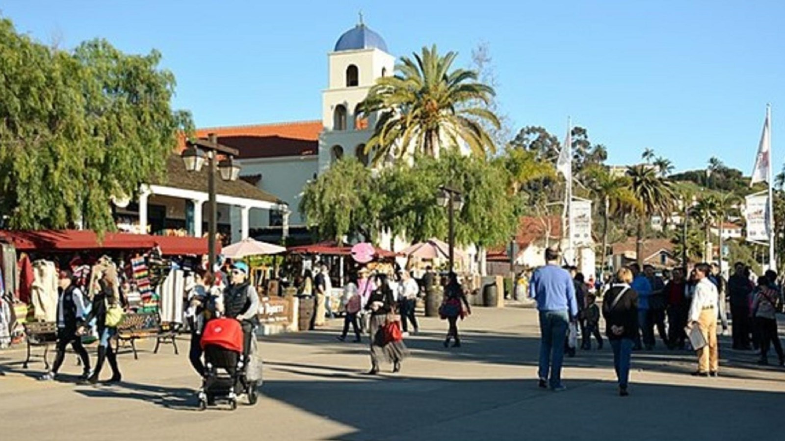 Numerous people walking down a busy street with vendors under canopies to its side.