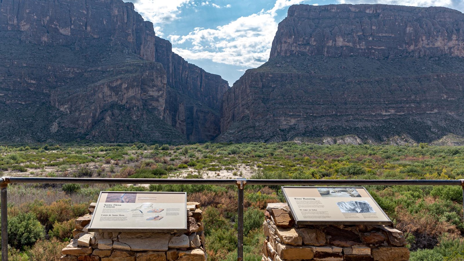 A metal frame on a rock pedestal holds a sign that discusses the formation of Santa Elena Canyon.
