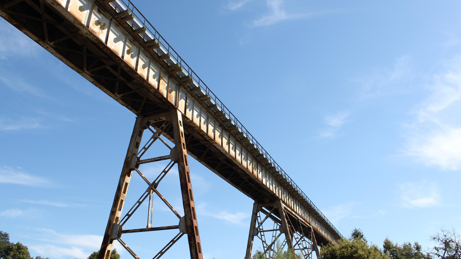 A train trestle (bridge) spans across the sky. Trees can be seen underneath. 