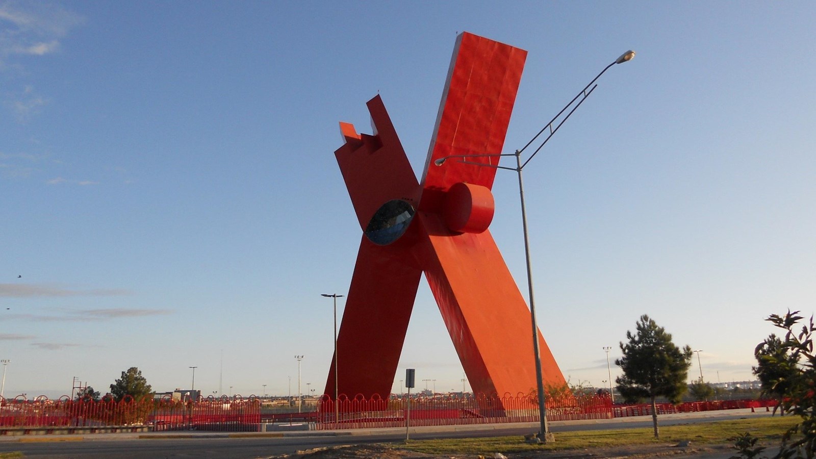 Image of red-orange x-shaped monument against blue sky