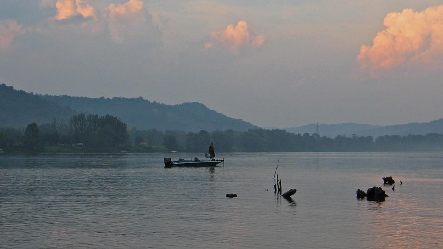 A person fishing from a small boat on a wide, calm river