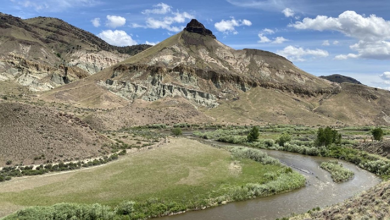 A pointed mountain with a river flowing in front through green fields