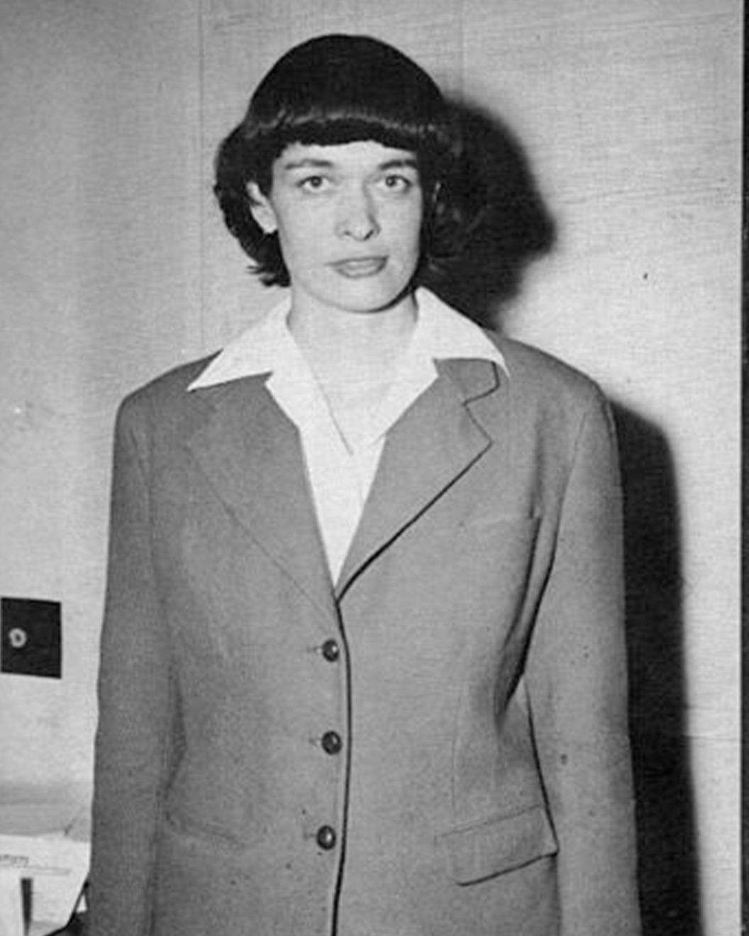 Black and white photo of a young woman standing in front of the camera.