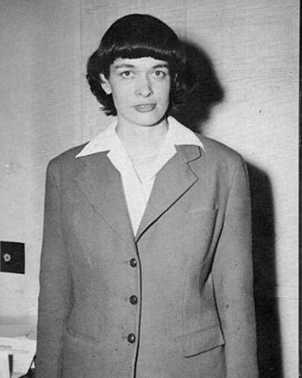 Black and white photo of a young woman standing in front of the camera.