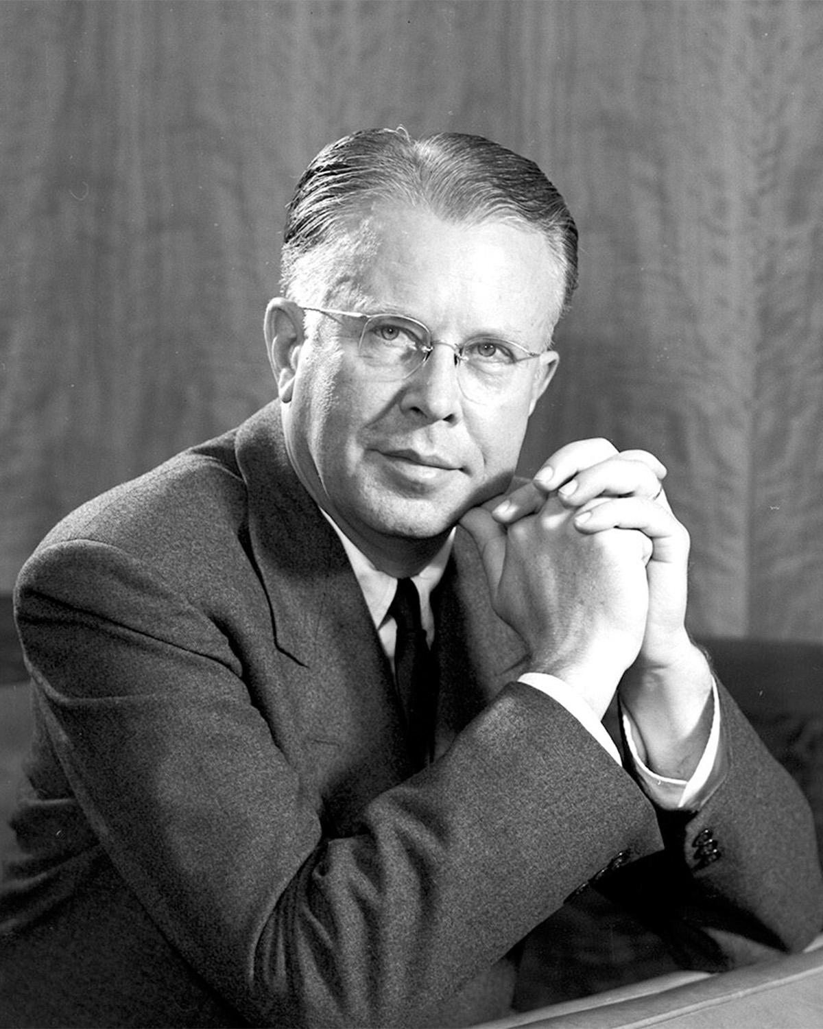 A black and white photo of a man in a suit and glasses.