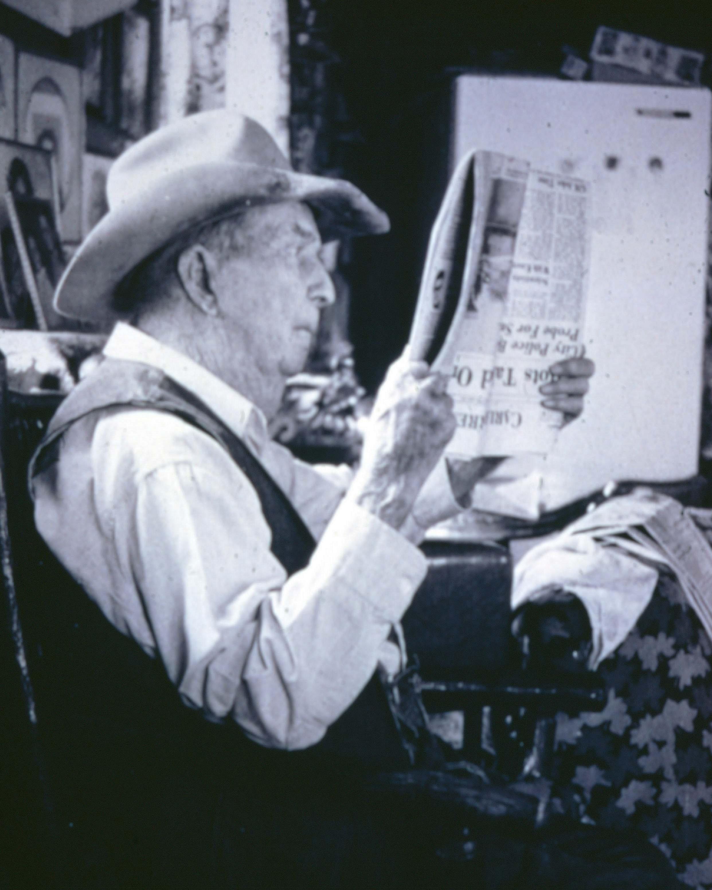 A man wearing a cowboy hat reads a newspaper