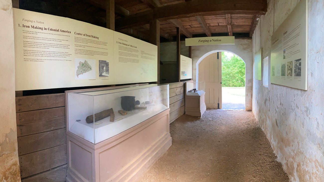 a space inside an historic stable with dirt floor artifact cases and exhibit panels
