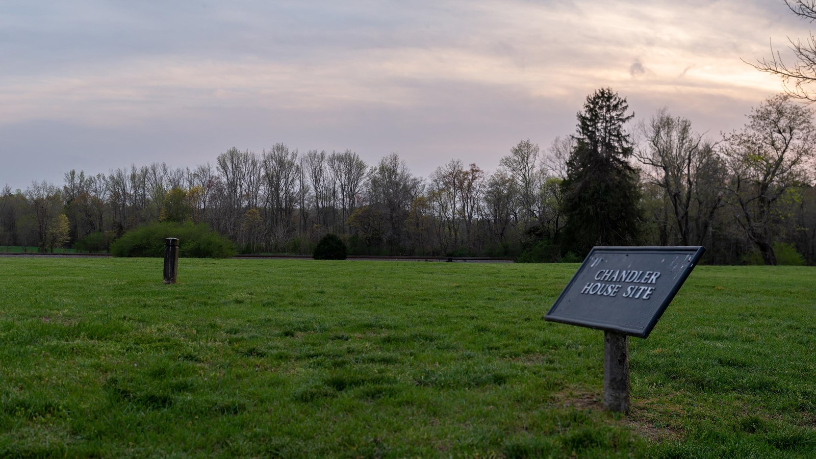 A sign that reads Chandler House Site, in a field with posts marking an outline where a house stood.