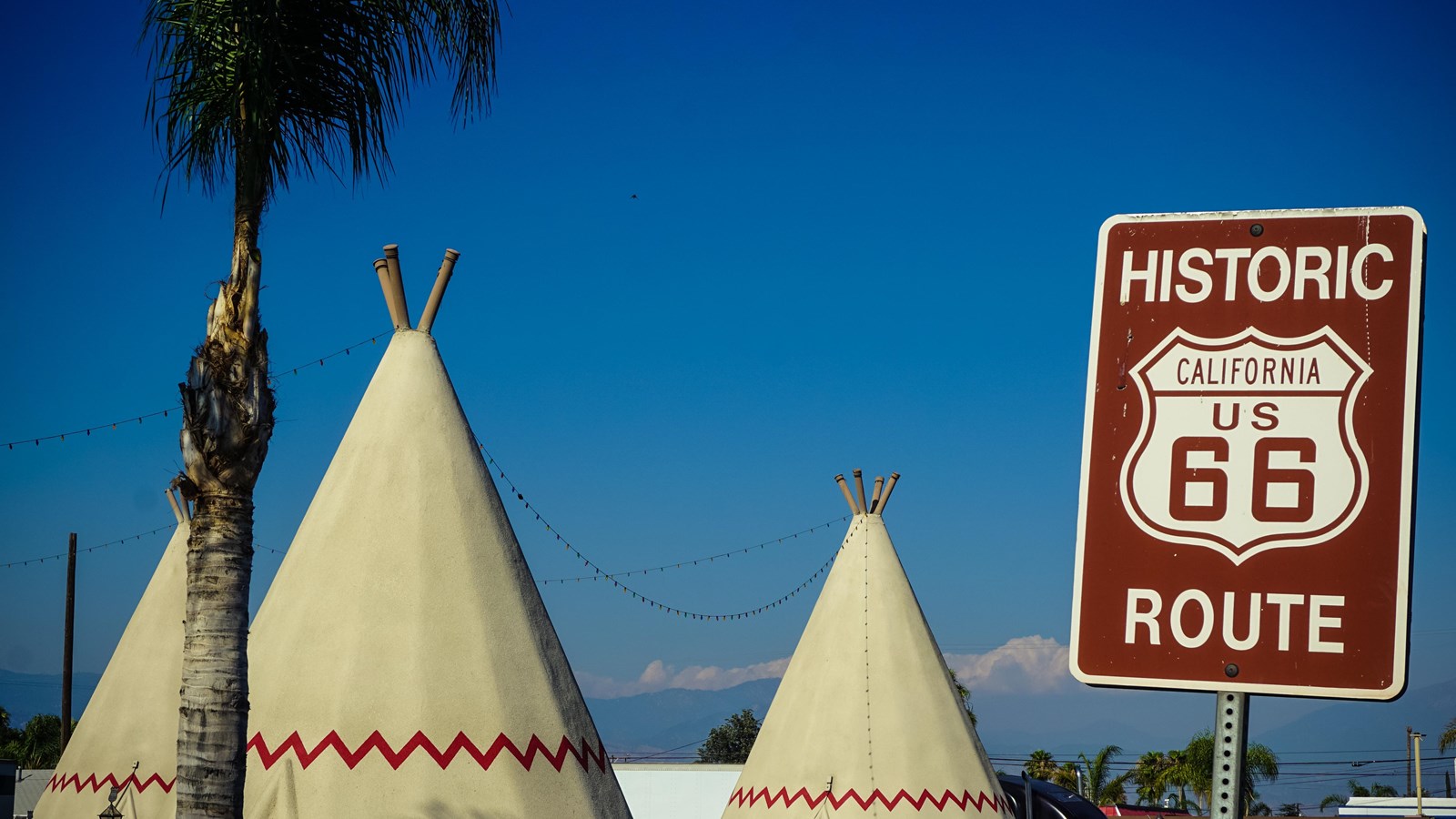 White cone shaped wigwams with red trim. A brown sign reads 