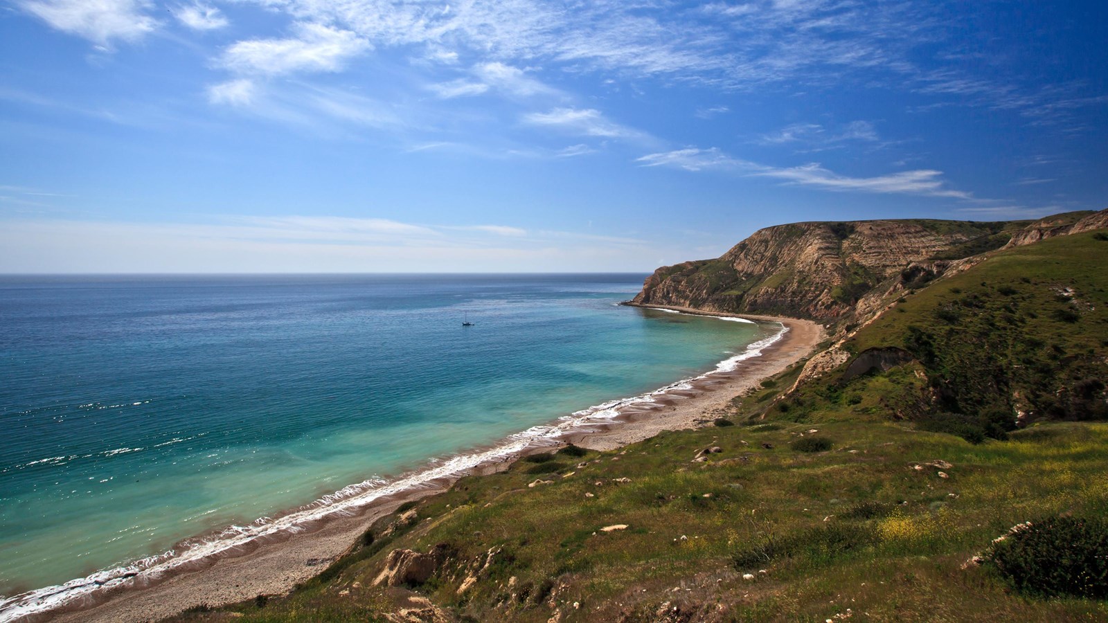 Crescent shaped harbor with sand and cobblestones leading to steep yellow banks in the distance. 