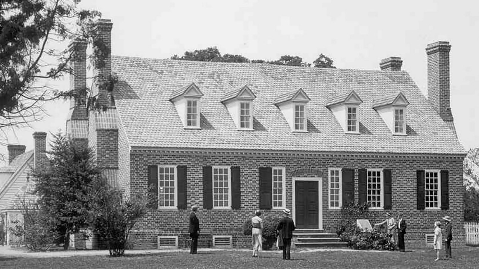 A black and white photo of a brick house and people walking up to the home
