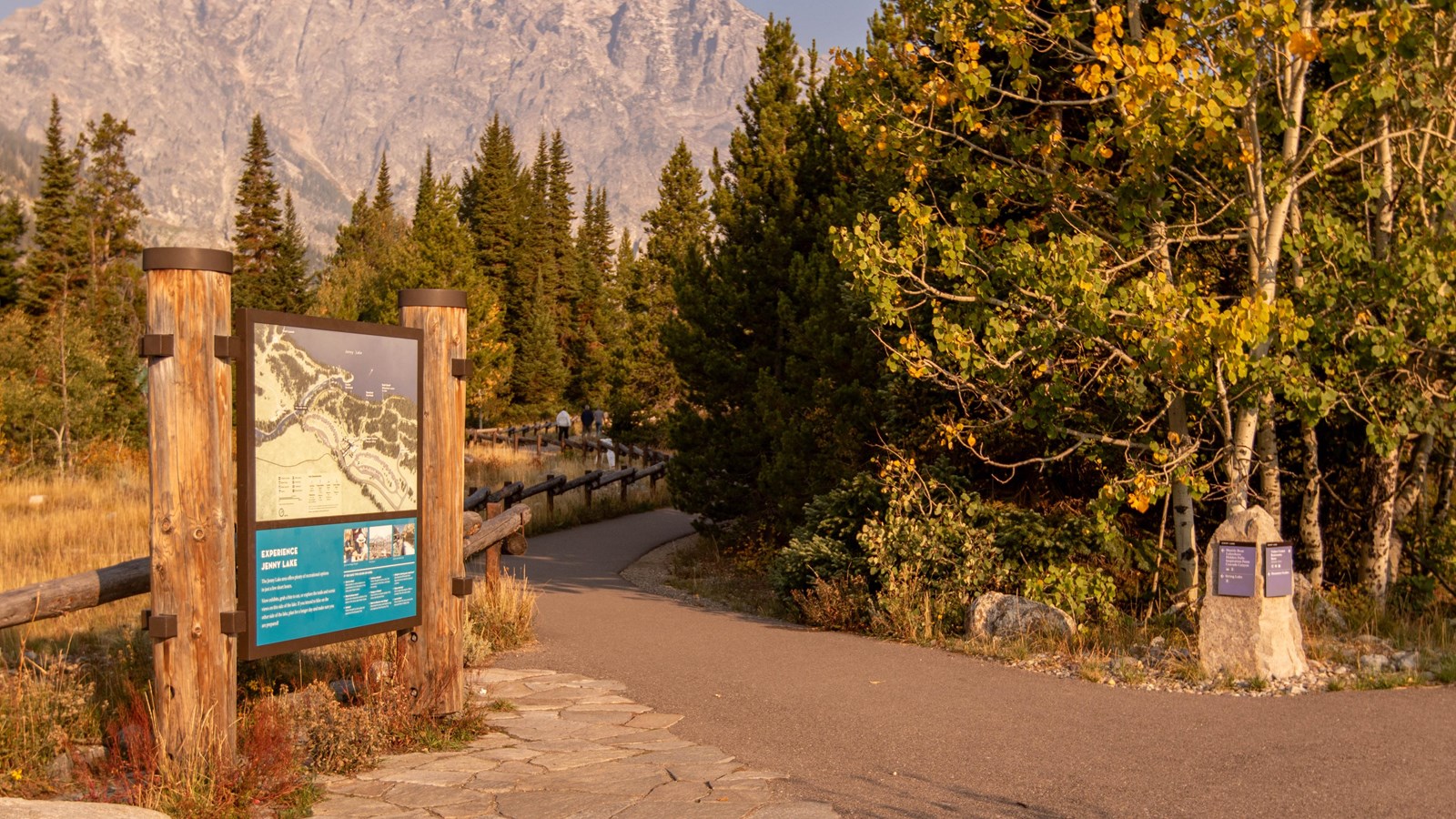 An informational sign with a large map along a paved pathway.