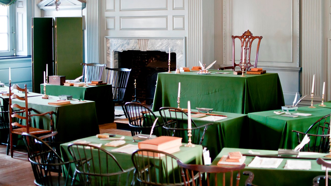 View of room interior showing two rows of tables facing a single chair and table on a dias.