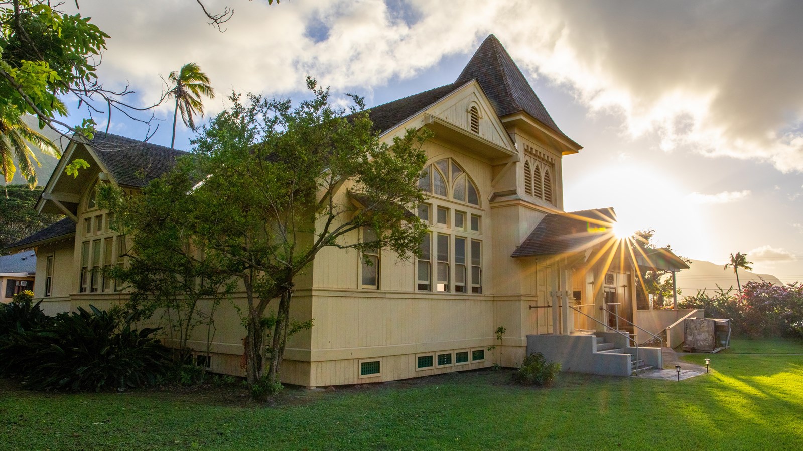 A church building, a green lawn, and the setting sun in the background.