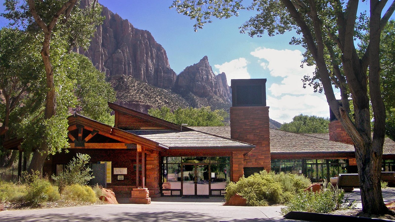Photo of a sandstone building under a cloudy blue sky, surrounded by green trees.