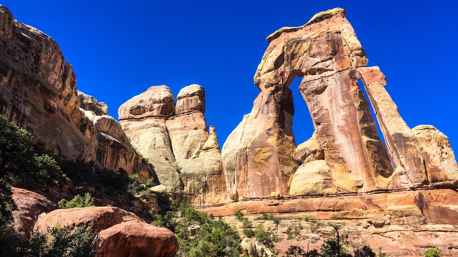 A large sandstone arch looms across the skyline on a bright, sunny blue sky day.