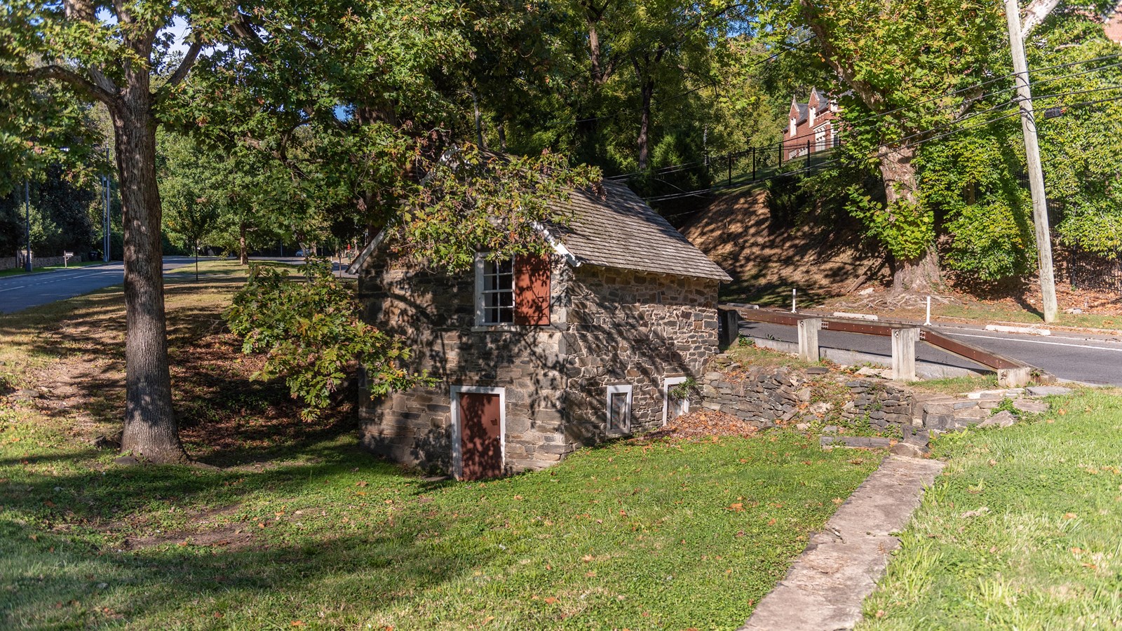 A stone house in front of a grassy field with woods in the background