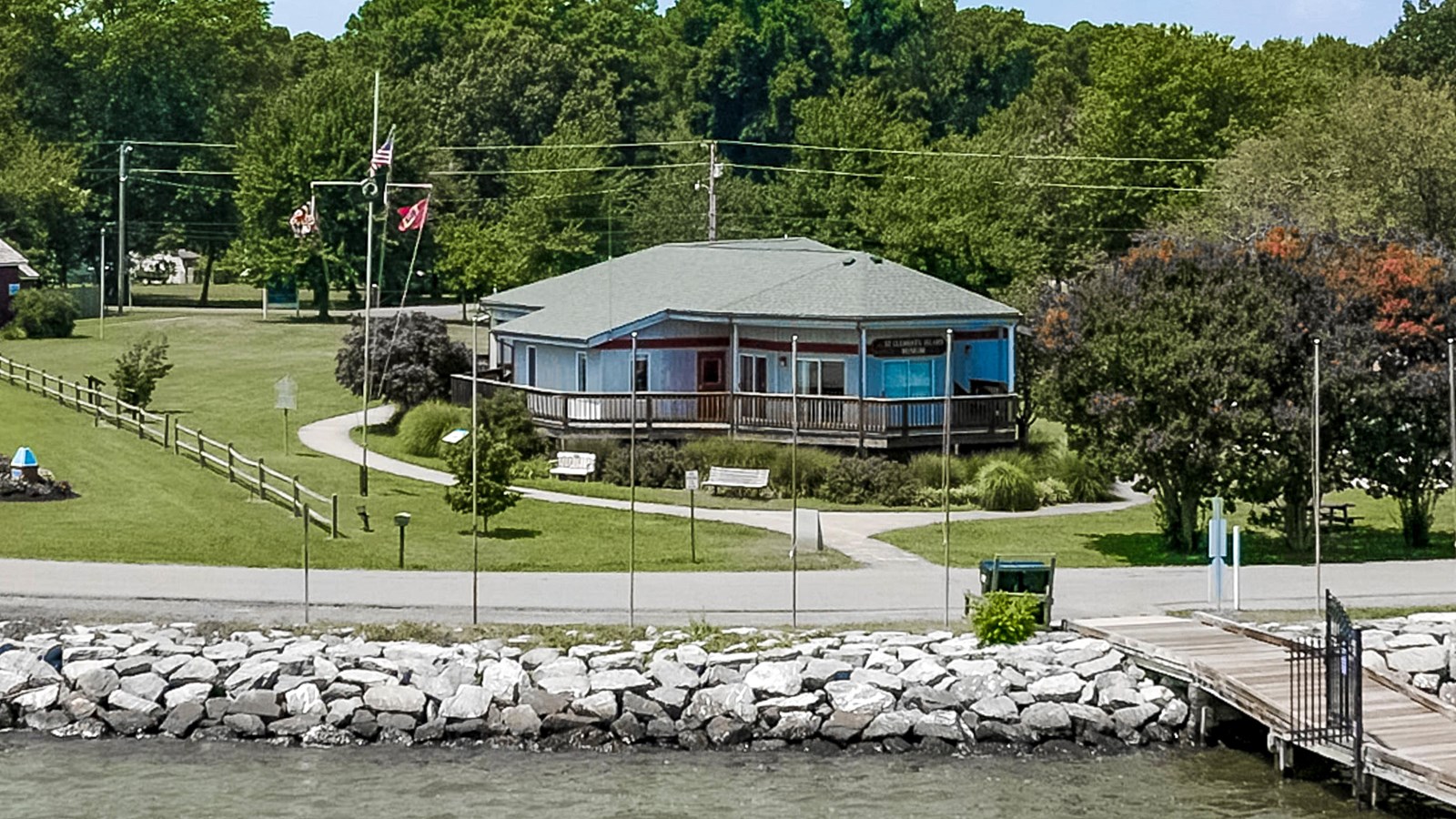 View of the waterfront with a blue building, wooden pier, and greenery.