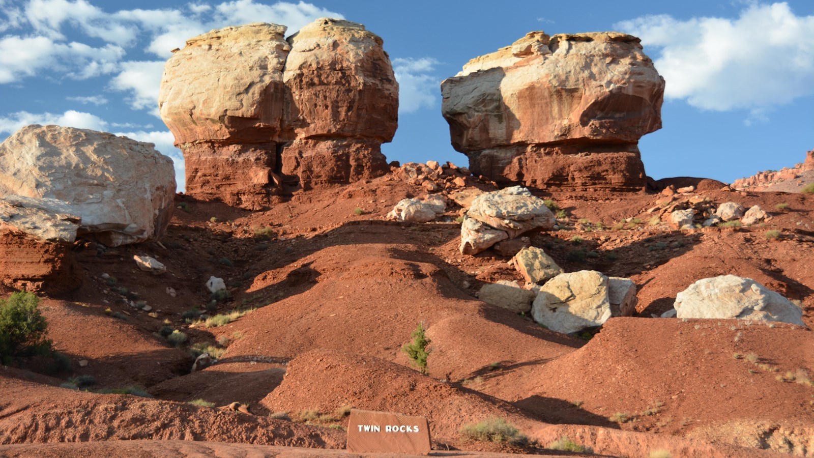 Two large elliptical white boulders sit on narrower pedestals of burnt orange rock atop a hill