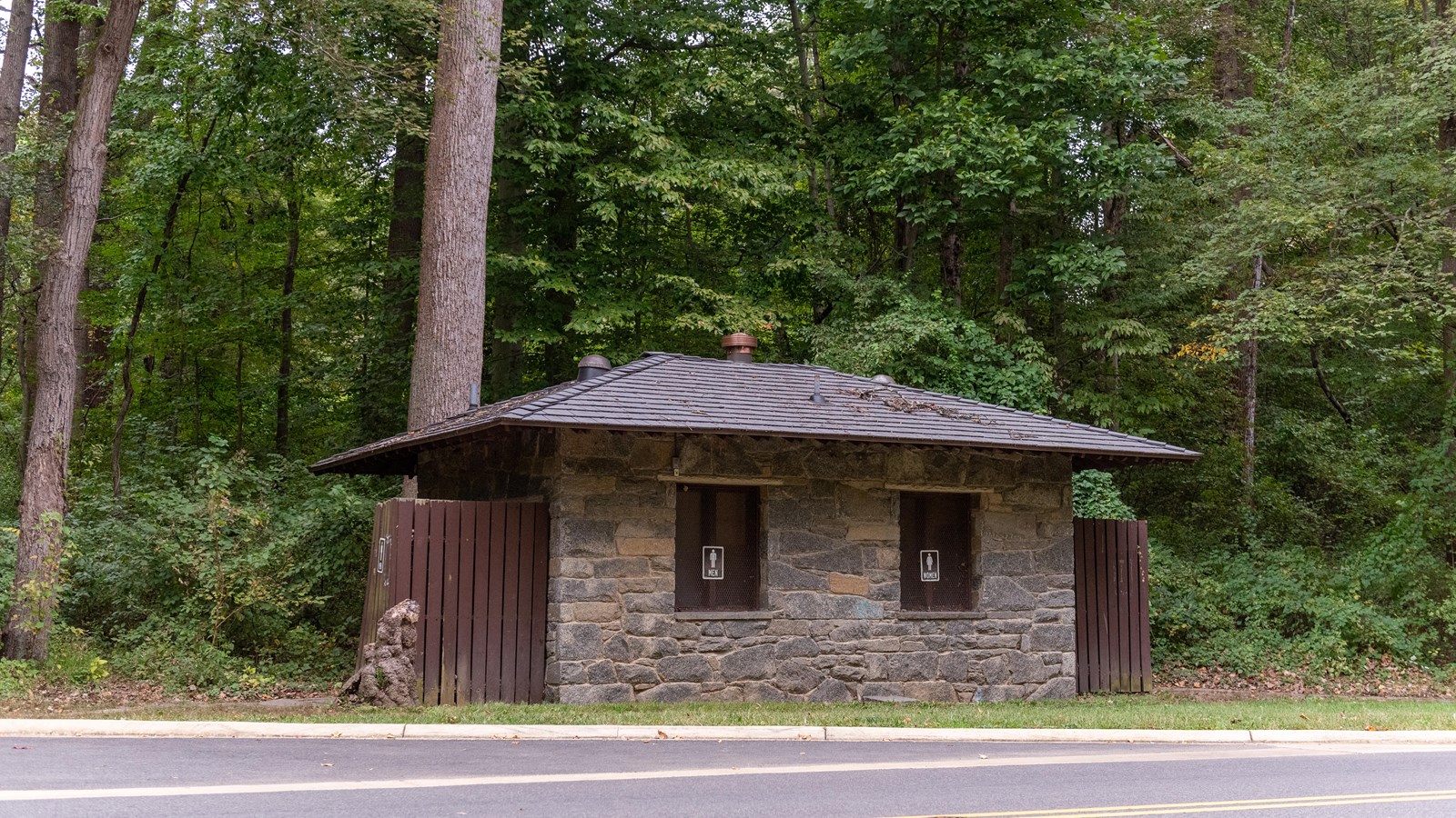 A small stone bathroom next to a road in the woods