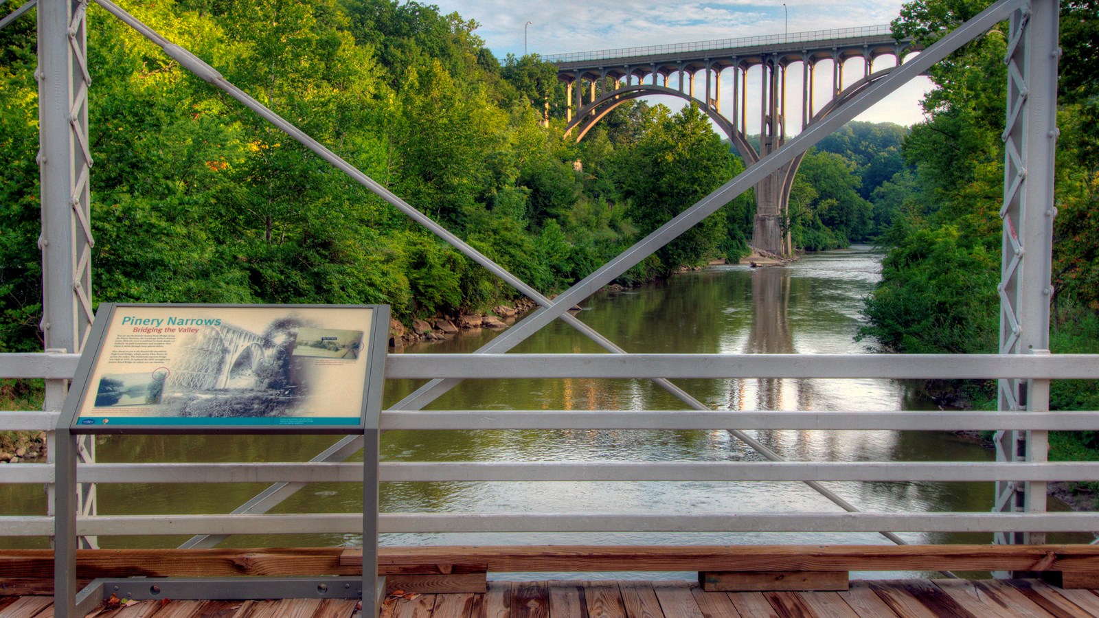 An iron bridge over a river with Pinery Narrows panel showing a distant concrete bridge bring built.