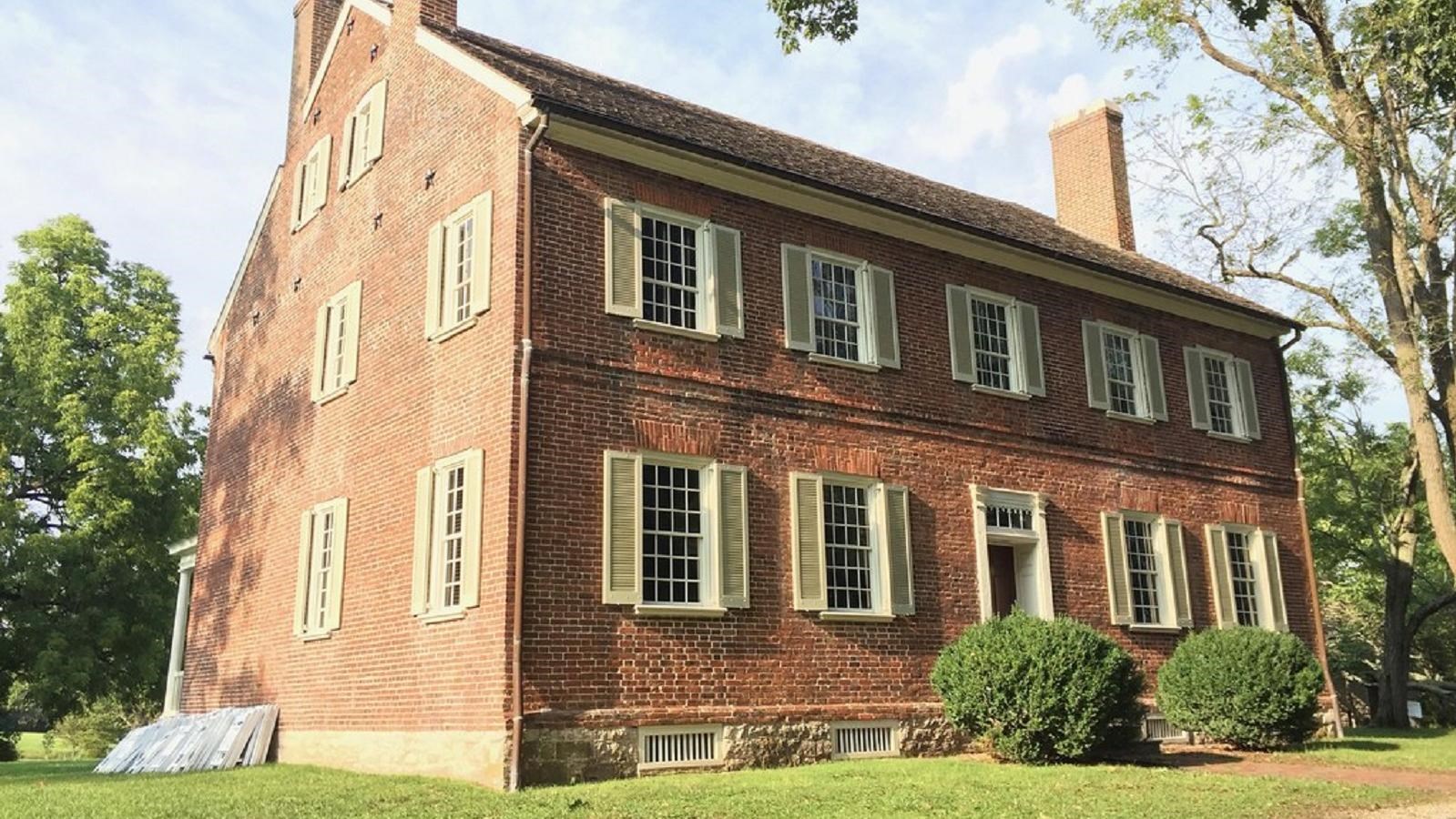 A 2-story red brick colonial house with white shutters amid a grassy lawn
