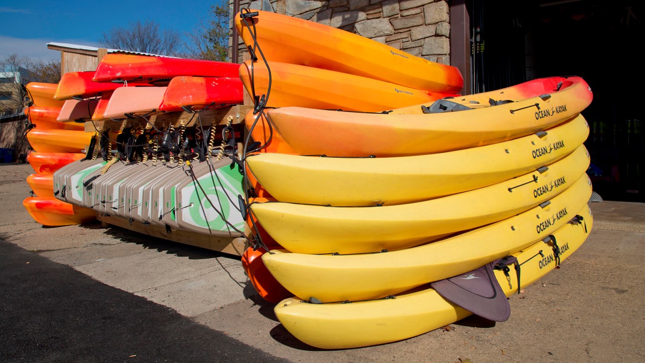 brightly colored kayaks, canoes and paddle boards are neatly stacked