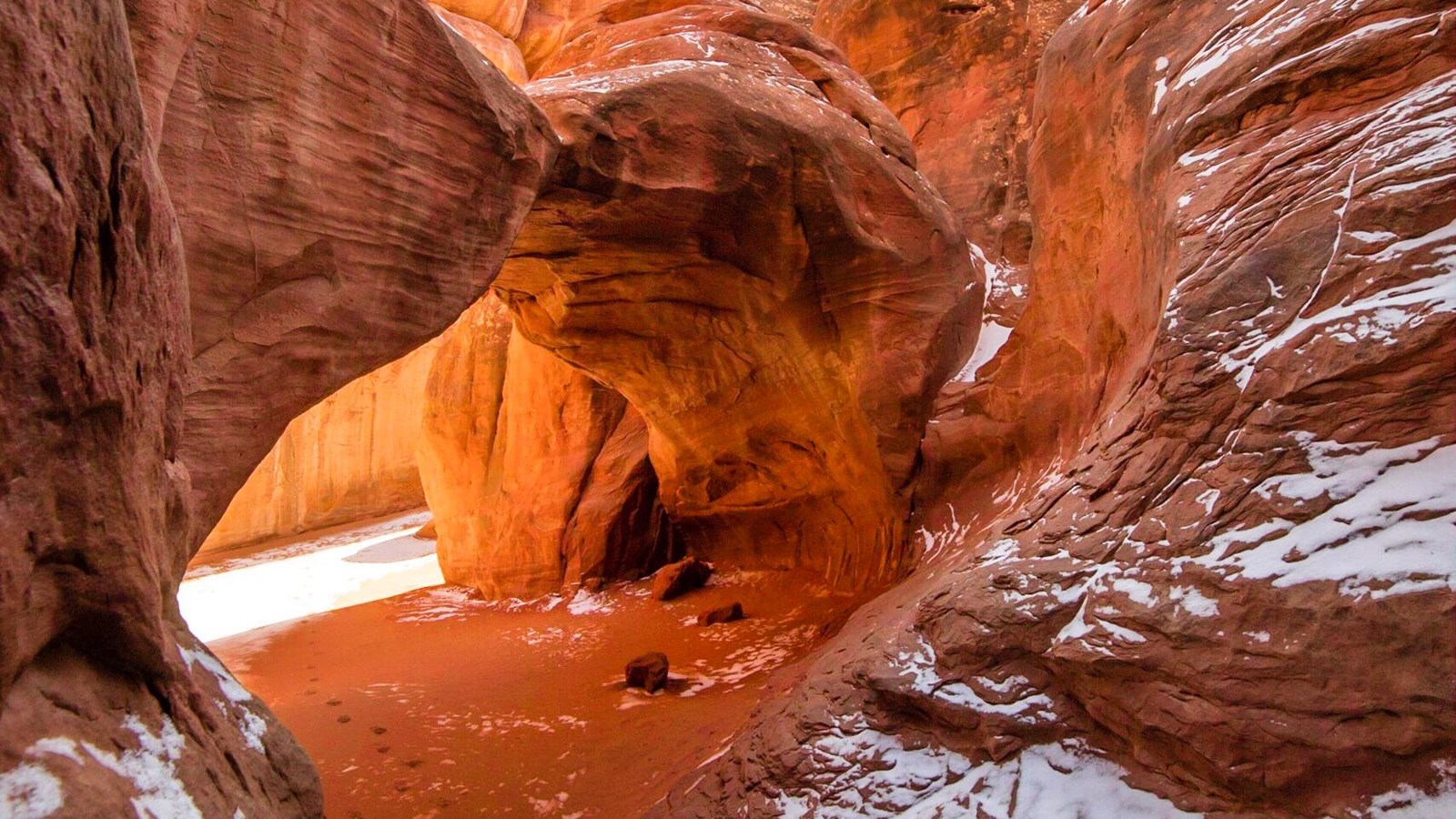 white snow on red sandstone, arch backdropped by more sandstone walls