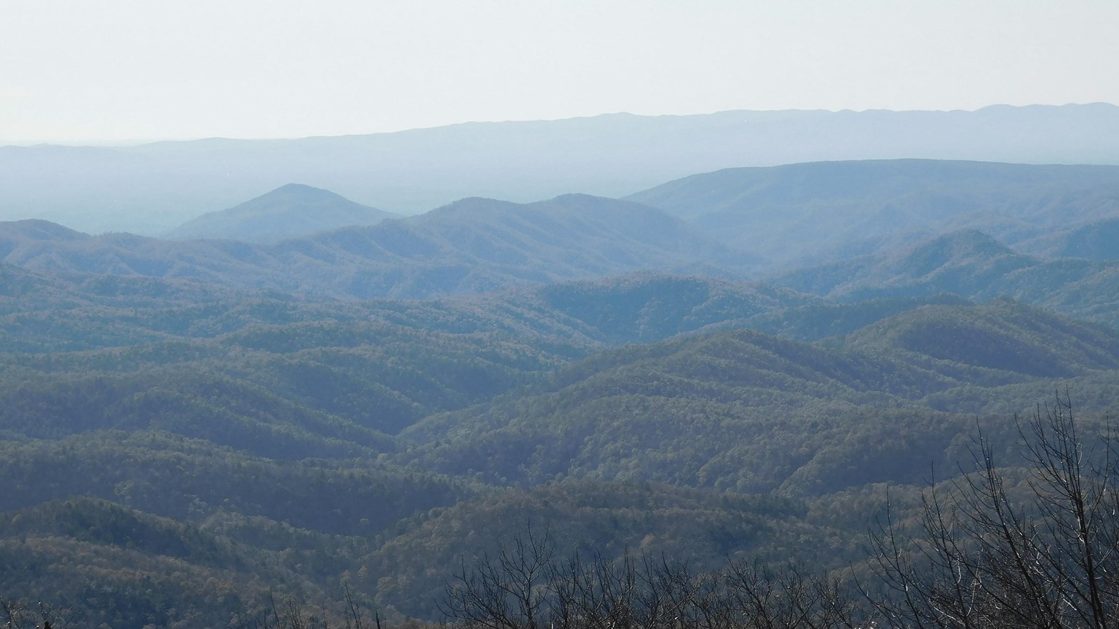 Blue tinted mountains stretch to the horizon under a pale winter sky