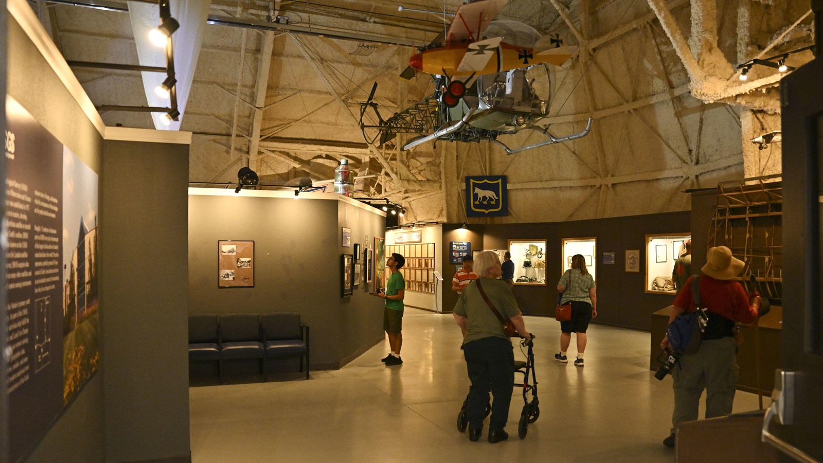 View of people exploring indoor museum exhibits. Aircraft are mounted on the ceiling.